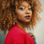 Striking portrait of a woman with curly hair, wearing a red jacket.