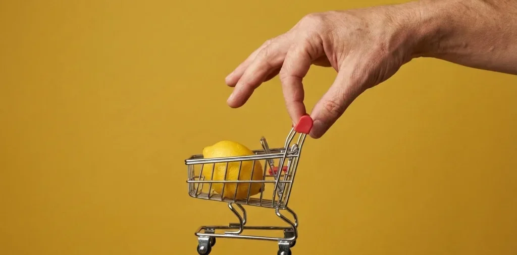 Mão segurando com as pontas dos dedos mini carrinho de compras com um limão dentro